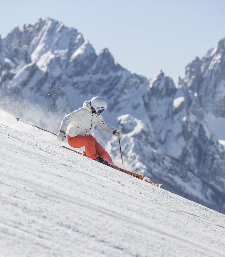 Ihr Hotel im Pustertal mit 5 Sternen: Alpen Tesitin Skifahrer in weißer Jacke und roter Hose fährt auf verschneiter Piste vor Bergkulisse