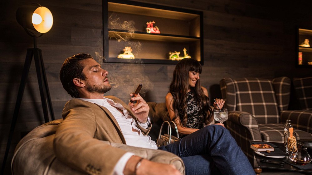 Le foto più belle dell’Alpen Tesitin Uomo rilassato sul divano con sigaro, donna che beve un cocktail in lounge accogliente
