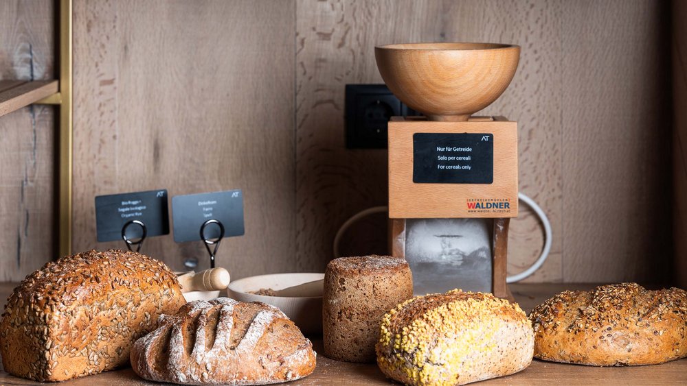 Le foto più belle dell’Alpen Tesitin Varie tipologie di pane davanti a un mulino per cereali in una cucina di legno
