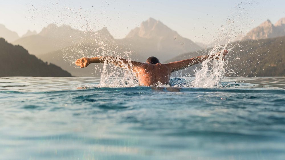 Le foto più belle dell’Alpen Tesitin Uomo che nuota in piscina con panorama montano sullo sfondo