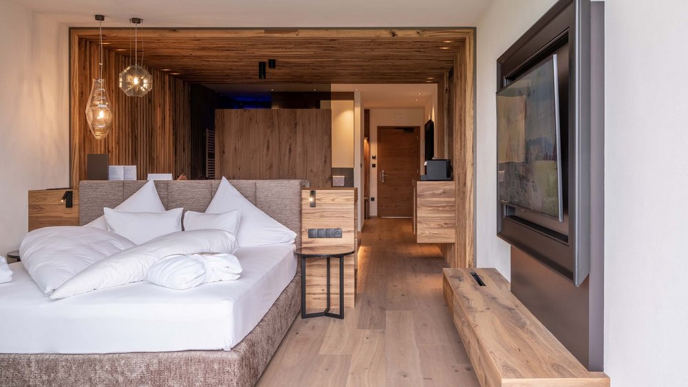 Le foto più belle dell’Alpen Tesitin Camera d'hotel moderna con letto, pannelli in legno e TV a parete