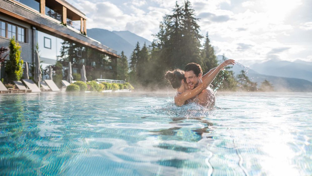 Le foto più belle dell’Alpen Tesitin Coppia che si abbraccia ridendo in piscina con vista sulle montagne