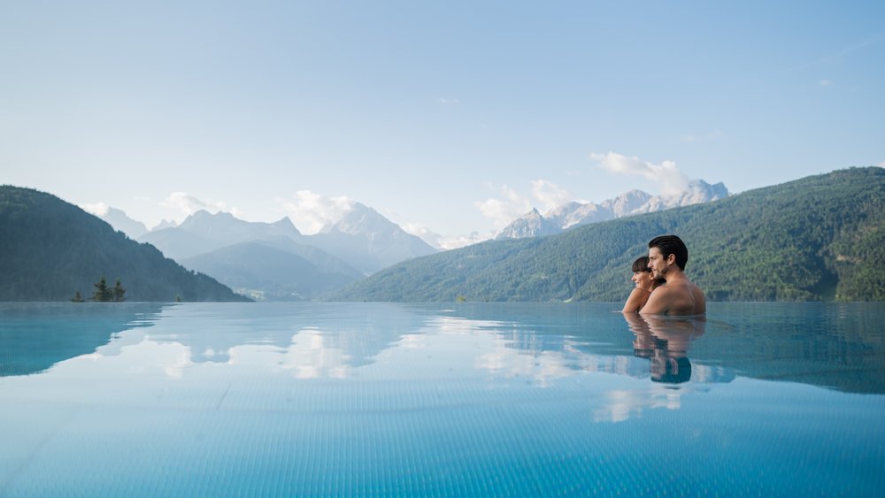 Le foto più belle dell’Alpen Tesitin Coppia rilassata in piscina a sfioro con vista sulle montagne e cielo blu