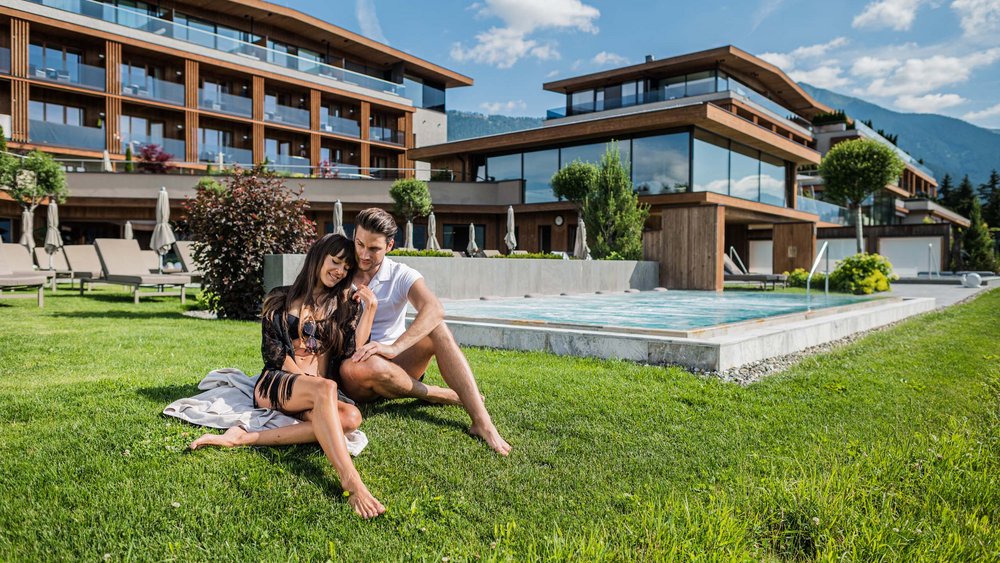 Le foto più belle dell’Alpen Tesitin Coppia rilassata su prato davanti a edificio moderno con piscina