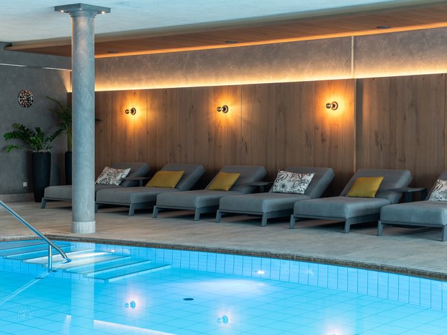 Your hotel in Val Pusteria/Pustertal with pool oasis Modern relaxation area with loungers by a lit indoor swimming pool