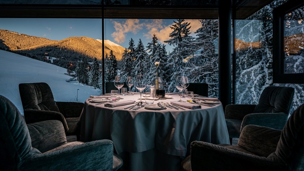 Le foto più belle dell’Alpen Tesitin Tavolo elegante apparecchiato davanti a una finestra panoramica con montagne innevate al tramonto