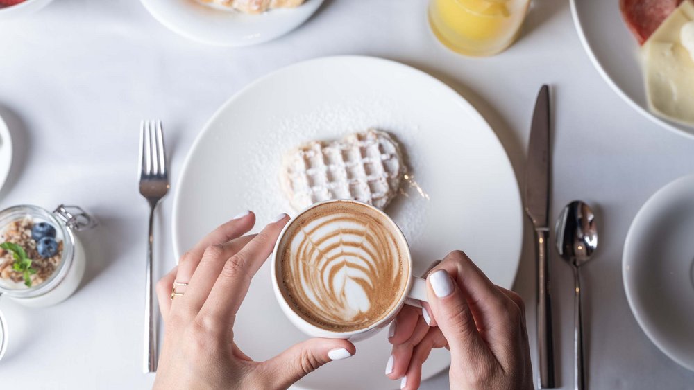 Le foto più belle dell’Alpen Tesitin Donna tiene tazza con latte art sopra piatto con waffle e colazione