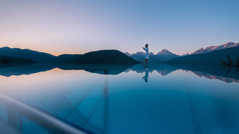 Le foto più belle dell’Alpen Tesitin Donna in accappatoio sul bordo di una piscina a sfioro con vista sulle montagne al tramonto