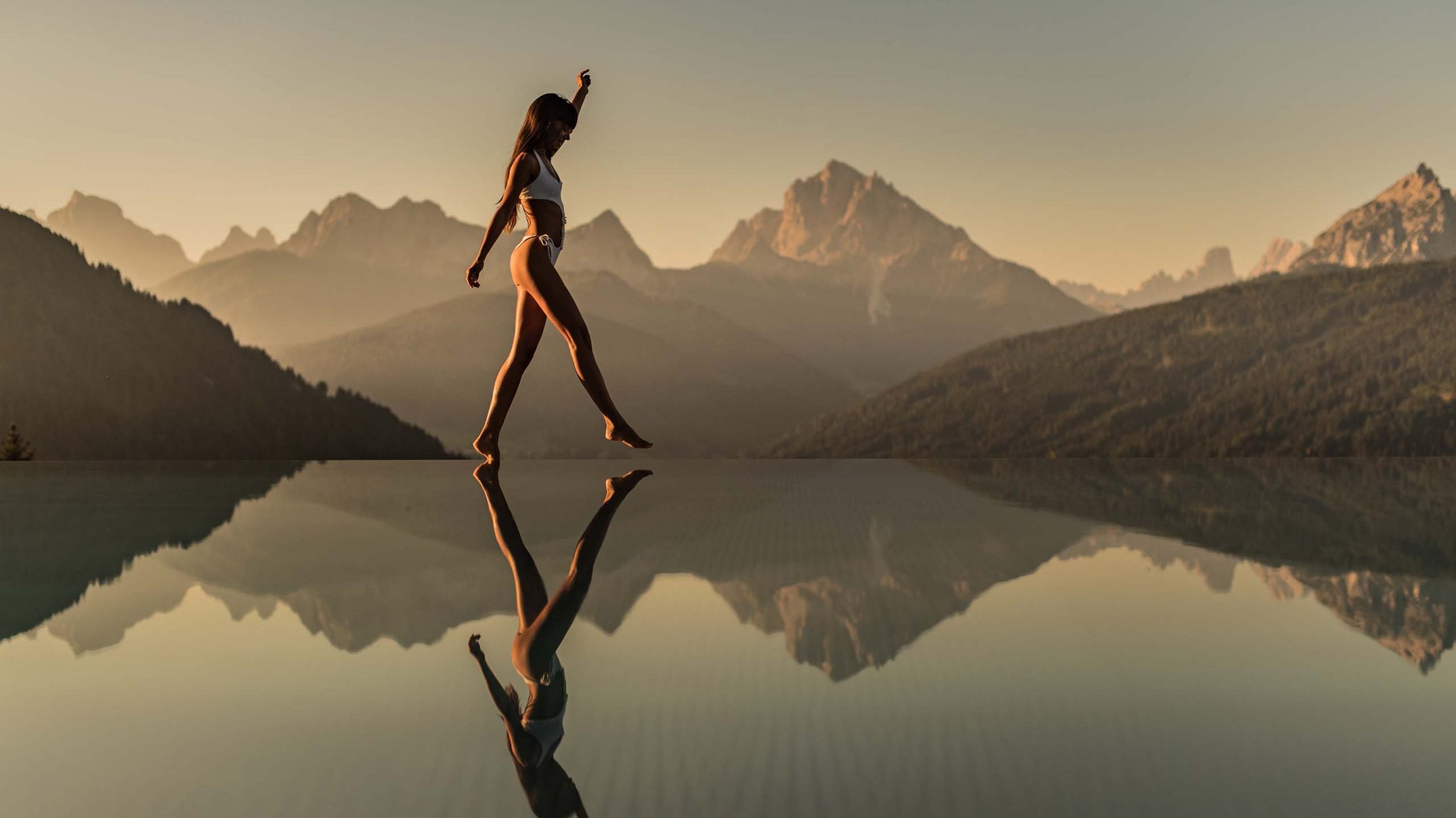 Ihr Hotel im Pustertal mit 5 Sternen: Alpen Tesitin Frau im Bikini geht am Rand eines Infinity-Pools mit Bergpanorama