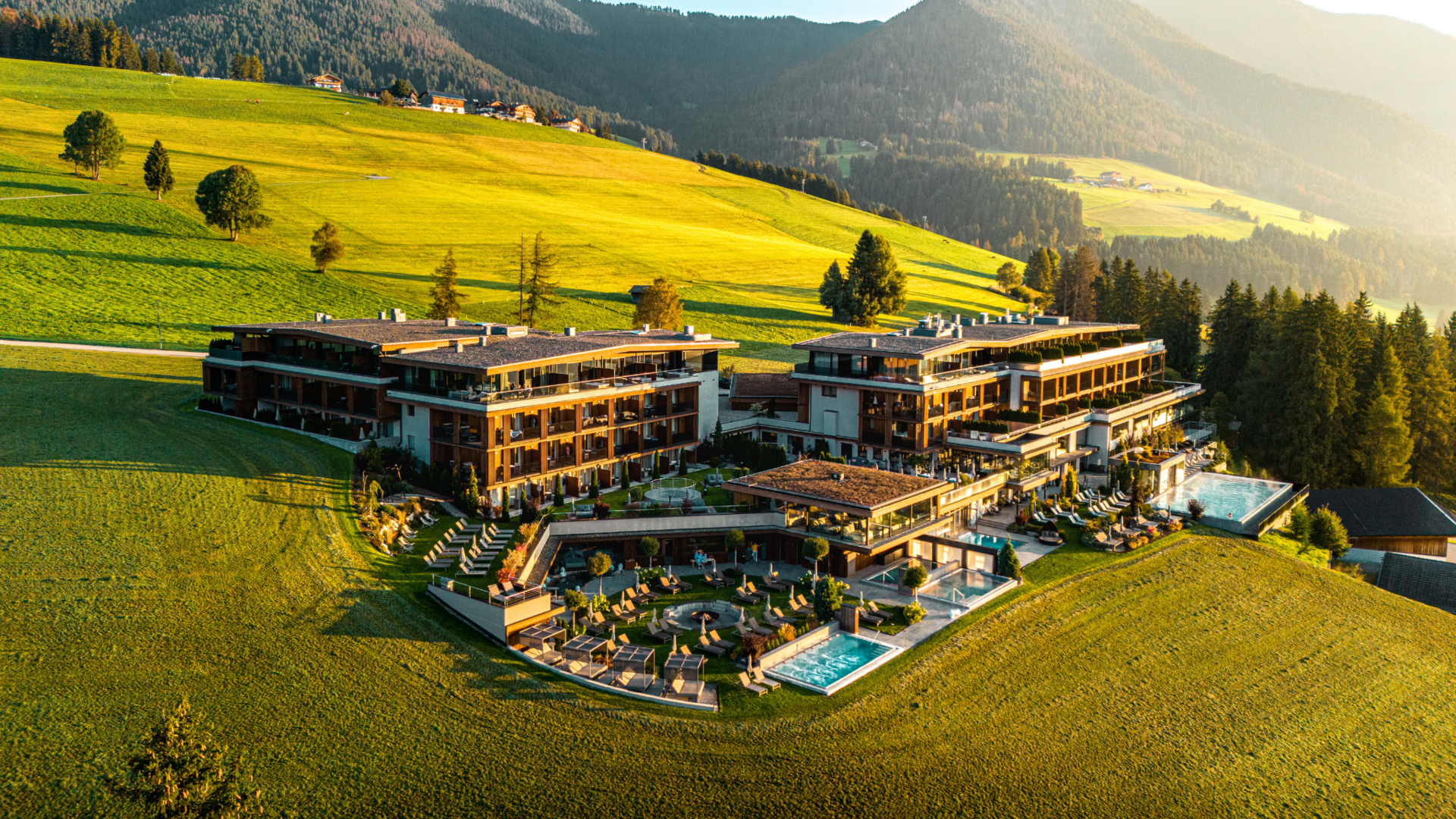 Ihr Hotel im Pustertal mit 5 Sternen: Alpen Tesitin Luxushotel mit Pool auf grünem Hügel vor bewaldeten Bergen im Sonnenuntergang