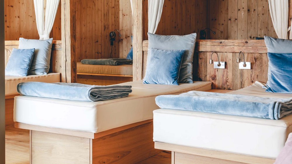 Le foto più belle dell’Alpen Tesitin Sala relax in legno con cuscini blu su lettini bianchi