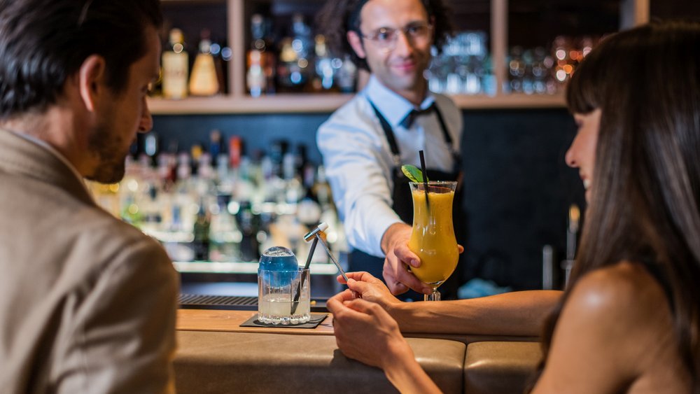 Le foto più belle dell’Alpen Tesitin Barista consegna un cocktail a una donna al bancone del bar