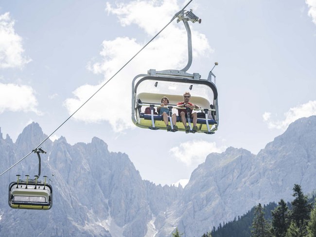 Alpen Tesitin, our hiking hotel in Val Pusteria/Pustertal Two people riding a chairlift with mountains in the background