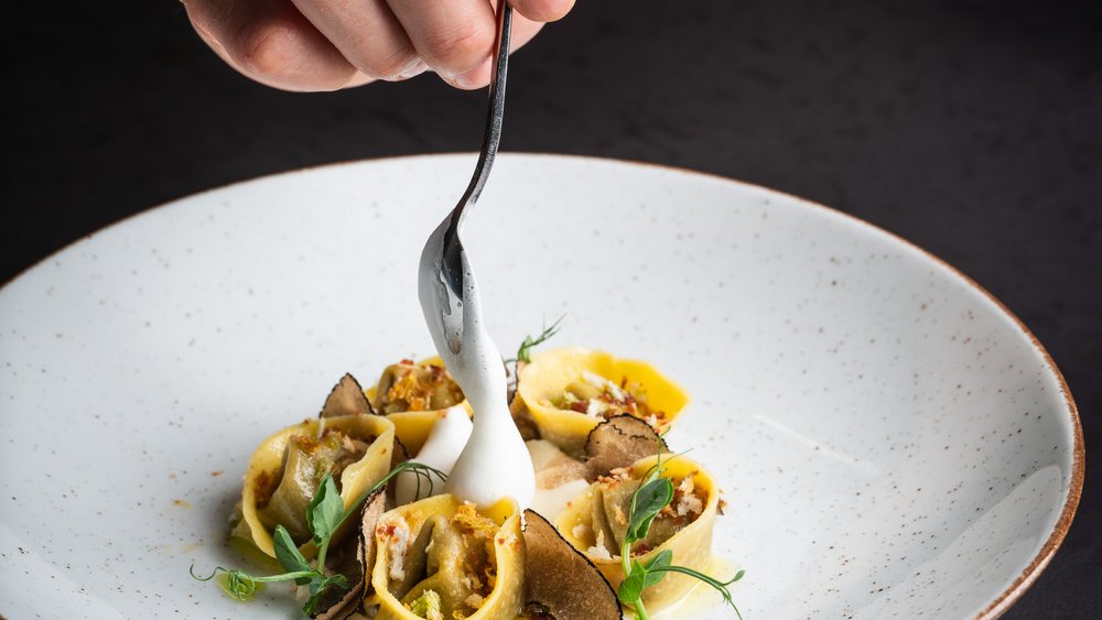 Le foto più belle dell’Alpen Tesitin Mano con cucchiaio versa salsa bianca su pasta ripiena con tartufo