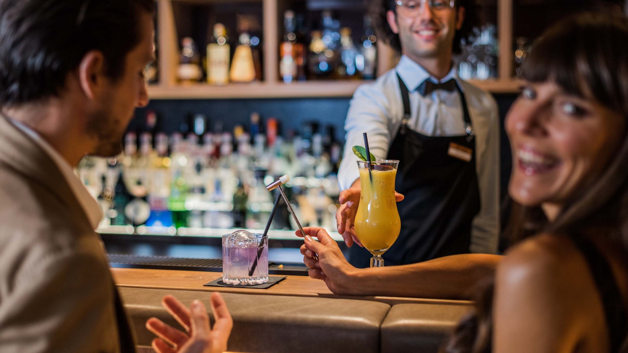 Ihr Hotel im Pustertal mit 5 Sternen: Alpen Tesitin Barkeeper serviert Drinks an ein lächelndes Paar in einer Bar