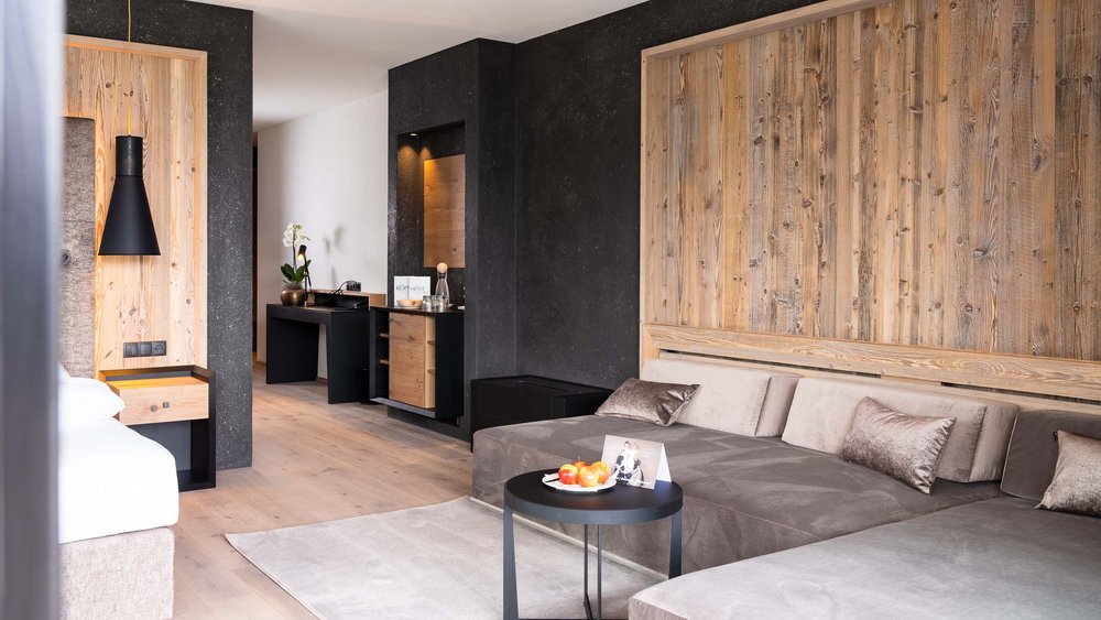 Le foto più belle dell’Alpen Tesitin Zona salotto moderna in camera d'hotel con divano, tavolo e parete in legno