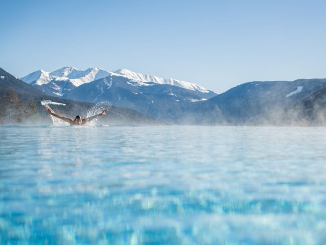 Your hotel in Val Pusteria/Pustertal with pool oasis Person swimming in heated pool with snowy mountains in the background