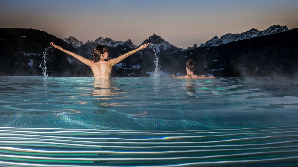 Le foto più belle dell’Alpen Tesitin Due persone in piscina riscaldata con vista sulle montagne al tramonto