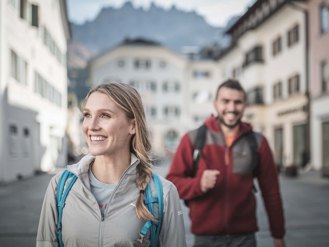 Alpen Tesitin, our hiking hotel in Val Pusteria/Pustertal Smiling woman with backpack in city, man blurred in the background