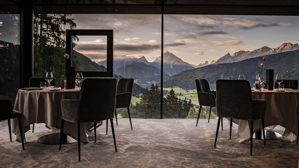 Le foto più belle dell’Alpen Tesitin Ristorante con tavoli davanti a grandi finestre e vista sulle montagne al tramonto
