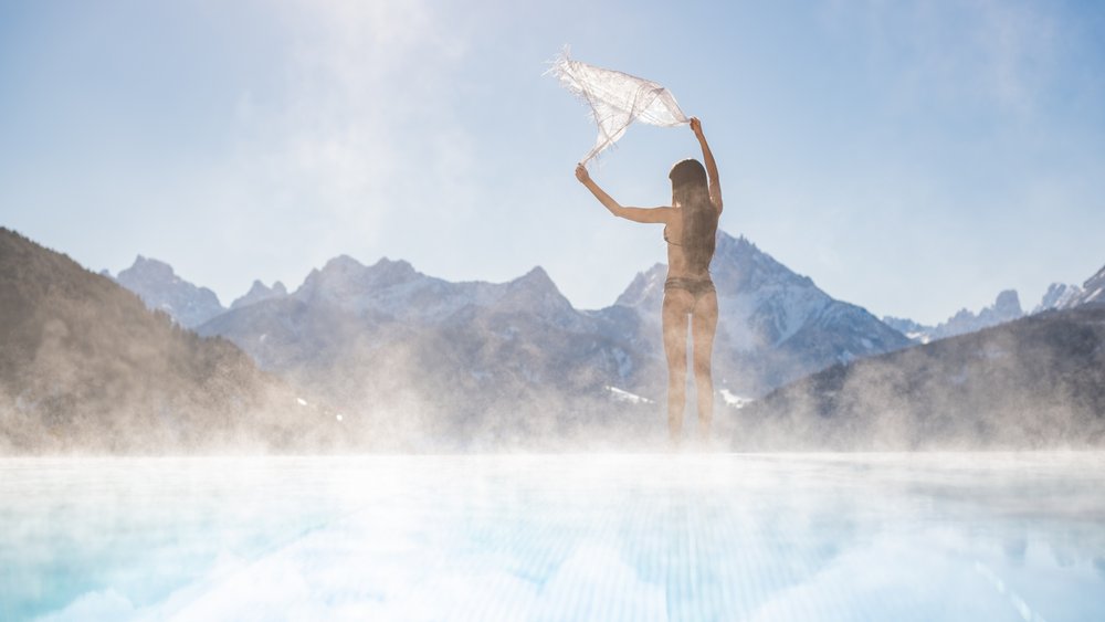 Le foto più belle dell’Alpen Tesitin Donna in costume da bagno con sciarpa vicino piscina fumante e montagne sullo sfondo