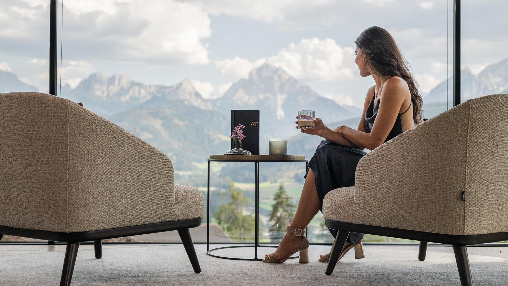 Ihr Hotel im Pustertal mit 5 Sternen: Alpen Tesitin Frau in elegantem Kleid sitzt drinnen mit Bergblick und Halbechtglas in der Hand