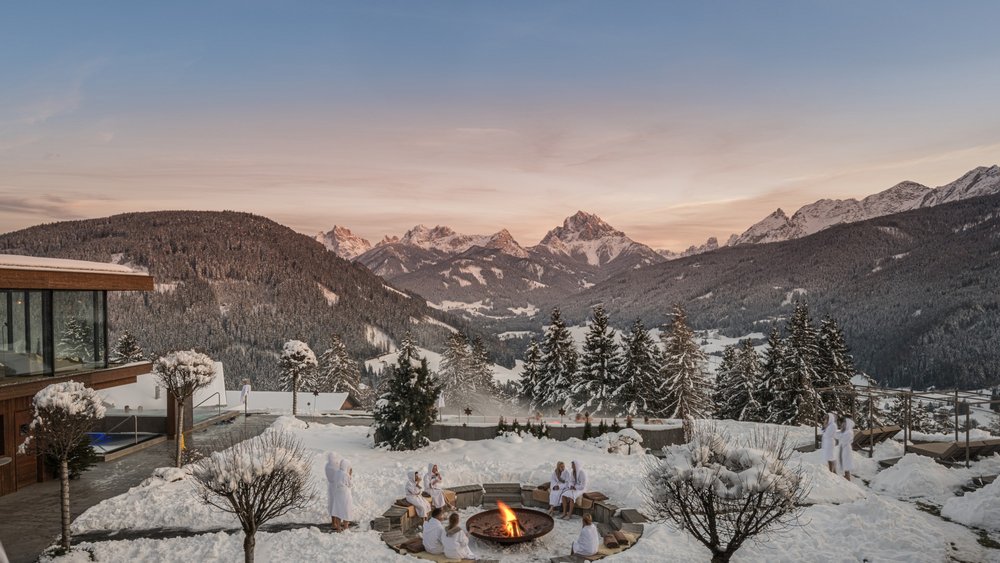 Le foto più belle dell’Alpen Tesitin Persone in accappatoio intorno a un fuoco all'aperto con montagne innevate sullo sfondo