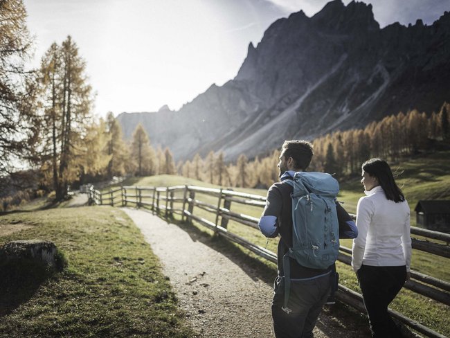 Alpen Tesitin, our hiking hotel in Val Pusteria/Pustertal Two hikers on a path beside wooden fence in autumn mountain landscape