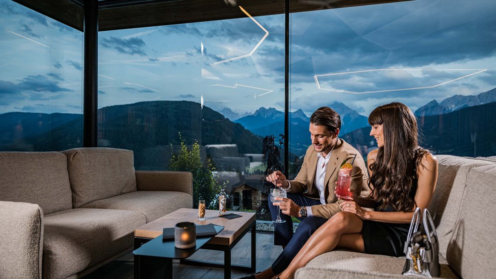 Le foto più belle dell’Alpen Tesitin Coppia beve cocktail in lounge con vista panoramica sulle montagne