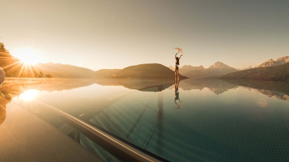 Le foto più belle dell’Alpen Tesitin Donna al bordo di una piscina infinity con tramonto e vista sulle montagne