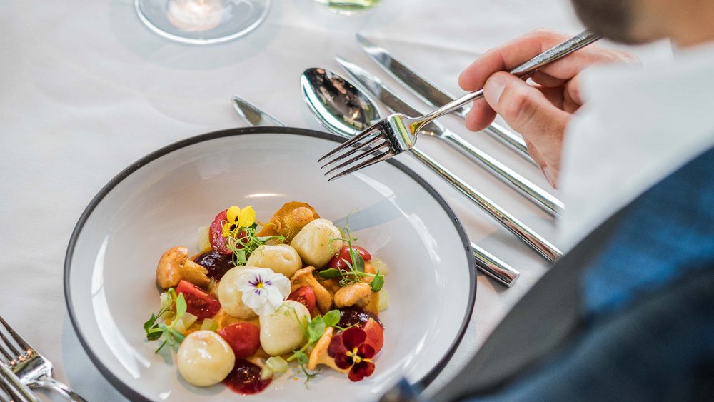 Le foto più belle dell’Alpen Tesitin Uomo che mangia piatto raffinato con funghi, pomodori e fiori commestibili in ristorante elegante