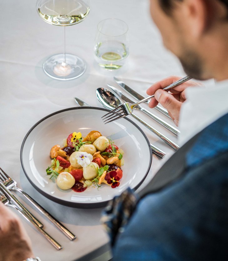 Ihr Hotel im Pustertal mit 5 Sternen: Alpen Tesitin Mann isst feines Gericht mit Pilzen, Tomaten und essbaren Blüten im edlen Restaurant
