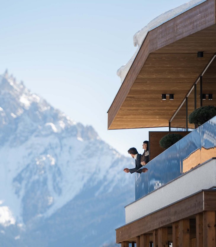 Ihr Hotel im Pustertal mit 5 Sternen: Alpen Tesitin Paar schaut von Balkon eines modernen Chalets auf schneebedeckten Berg