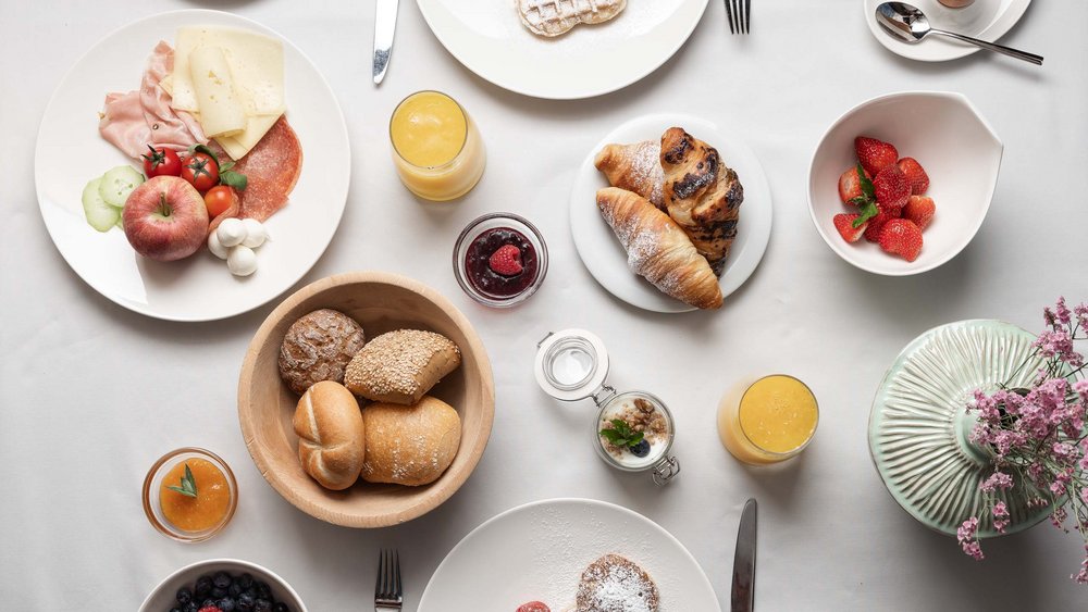 Le foto più belle dell’Alpen Tesitin Varie pietanze per colazione su tavolo bianco con caffè, frutta e dolci