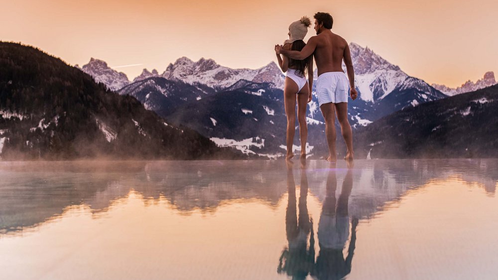 Le foto più belle dell’Alpen Tesitin Coppia in costume alla piscina riscaldata con vista sulle montagne innevate al tramonto