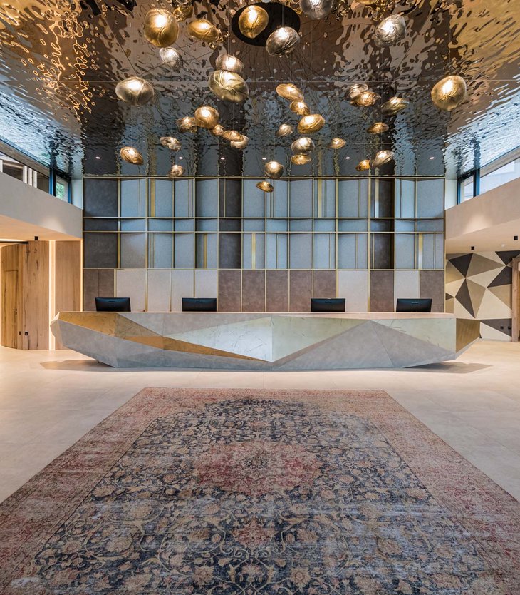 Alpen Tesitin: Your 5-star hotel in the Dolomites Modern lobby with geometric reception desk and sculptural ceiling lights