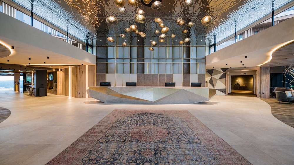 Le foto più belle dell’Alpen Tesitin Area reception moderna con bancone geometrico e lampade scultoree al soffitto