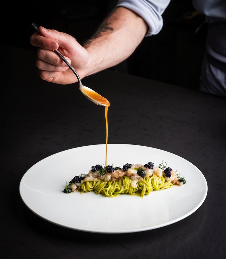 Ihr Hotel im Pustertal mit 5 Sternen: Alpen Tesitin Ein Koch gießt Sauce auf kunstvoll angerichtete Pasta mit Meeresfrüchten und Kaviar.