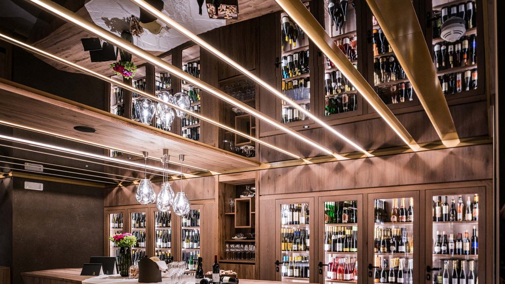 Le foto più belle dell’Alpen Tesitin Cantina moderna con scaffali illuminati e bancone in legno