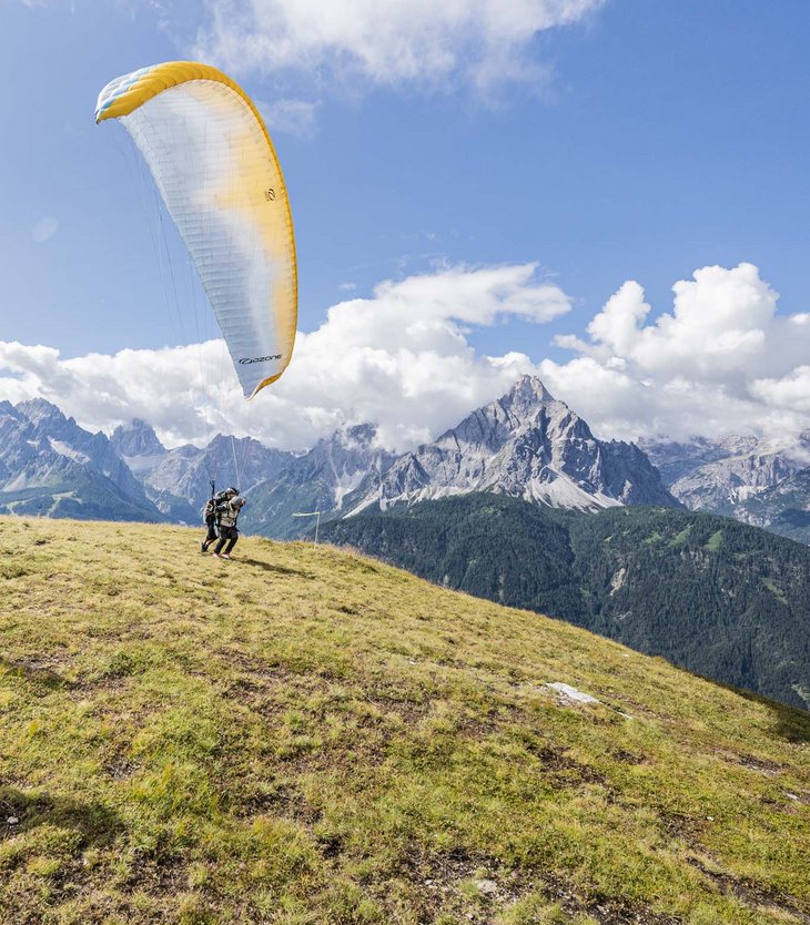 Action & adventure in Alta Pusteria/Hochpustertal People preparing for paragliding launch on a sunny mountain hillside