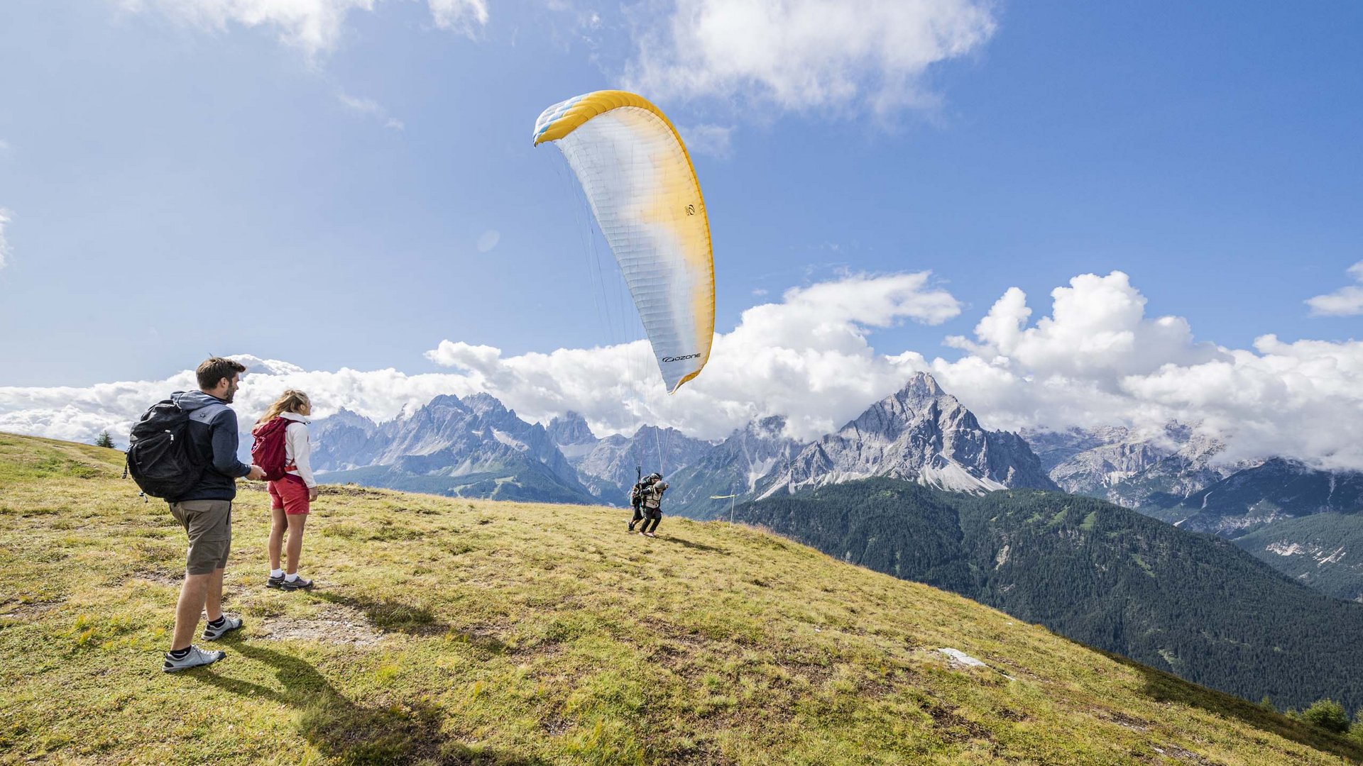 Action & adventure in Alta Pusteria/Hochpustertal People preparing for paragliding launch on a sunny mountain hillside