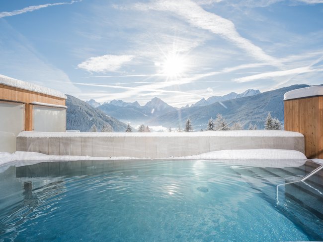 Your hotel in Val Pusteria/Pustertal with pool oasis Outdoor pool in snow with mountain view under bright sunny sky