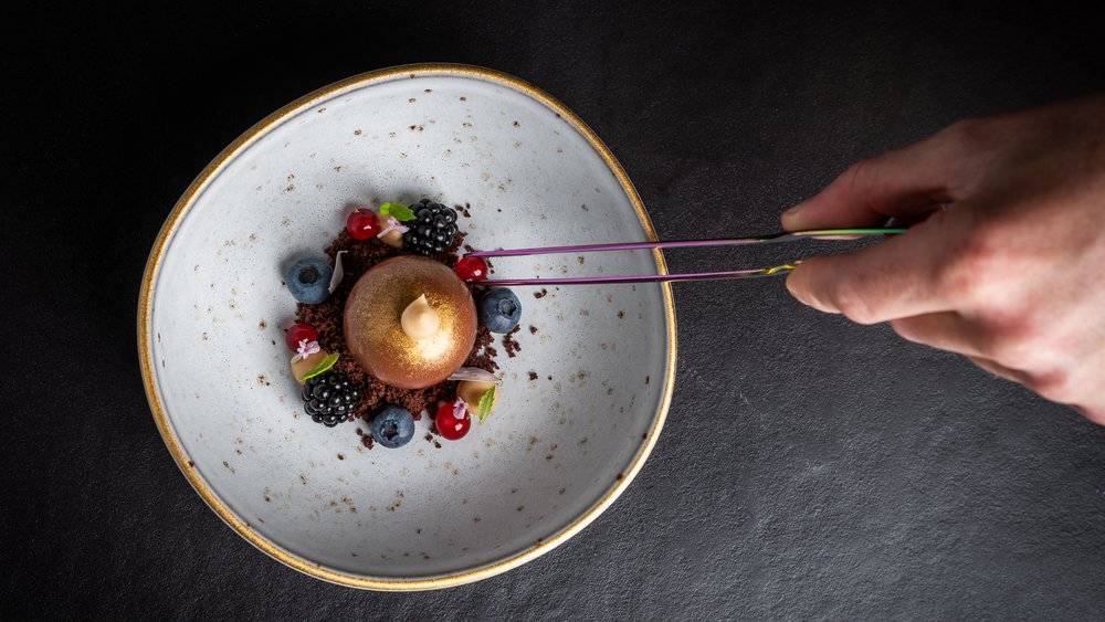 Le foto più belle dell’Alpen Tesitin Mano che posiziona una bacca su dessert artistico con bacche e crema
