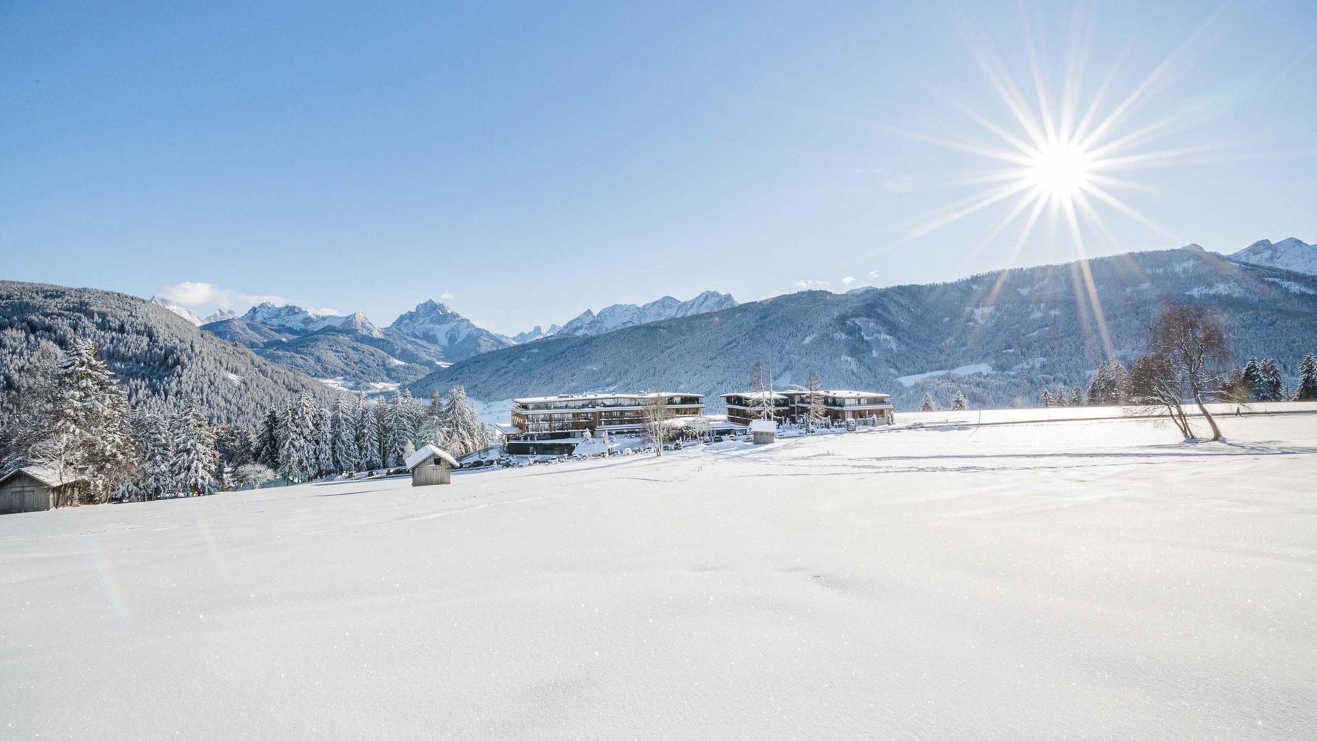 Ihr Hotel im Pustertal mit 5 Sternen: Alpen Tesitin Schneebedeckte Landschaft mit Bergen, Bäumen und Gebäuden unter strahlender Sonne