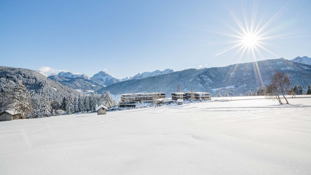 Le foto più belle dell’Alpen Tesitin Paesaggio innevato con montagne, alberi e edifici sotto un sole brillante