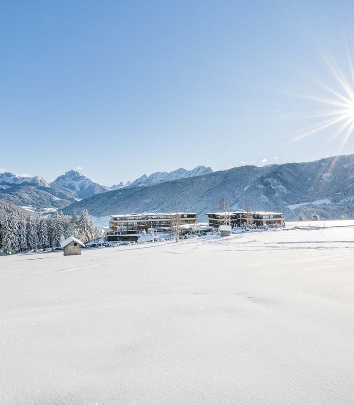 Ihr Hotel im Pustertal mit 5 Sternen: Alpen Tesitin Schneebedeckte Landschaft mit Bergen, Bäumen und Gebäuden unter strahlender Sonne