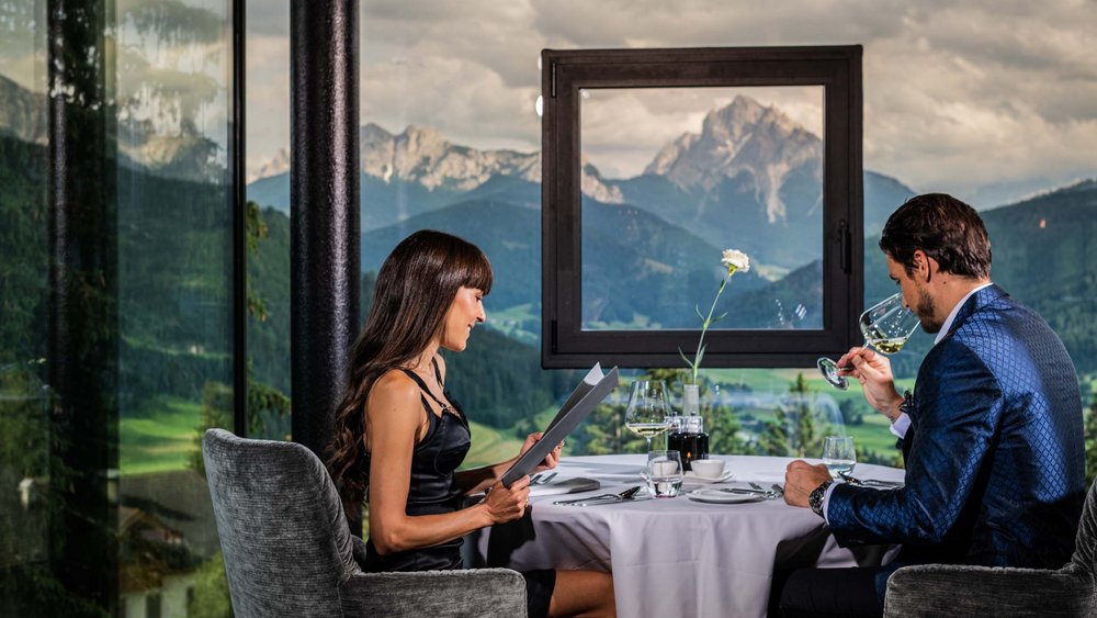 Le foto più belle dell’Alpen Tesitin Coppia che cena con vista sulle montagne attraverso finestra in ristorante elegante
