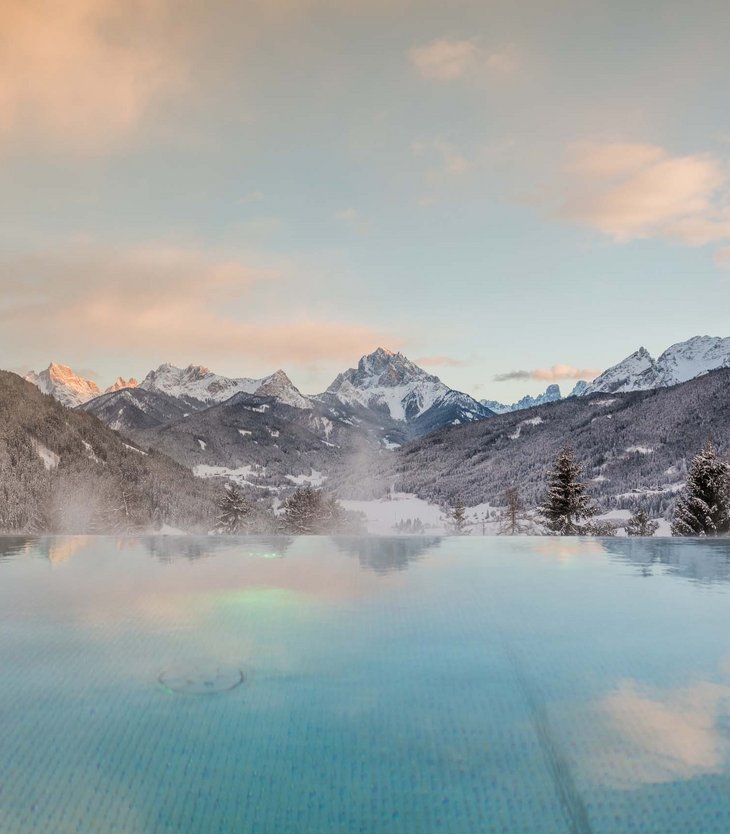 Ihr Hotel im Pustertal mit 5 Sternen: Alpen Tesitin Ein beheizter Pool mit Blick auf schneebedeckte Berge bei Sonnenuntergang