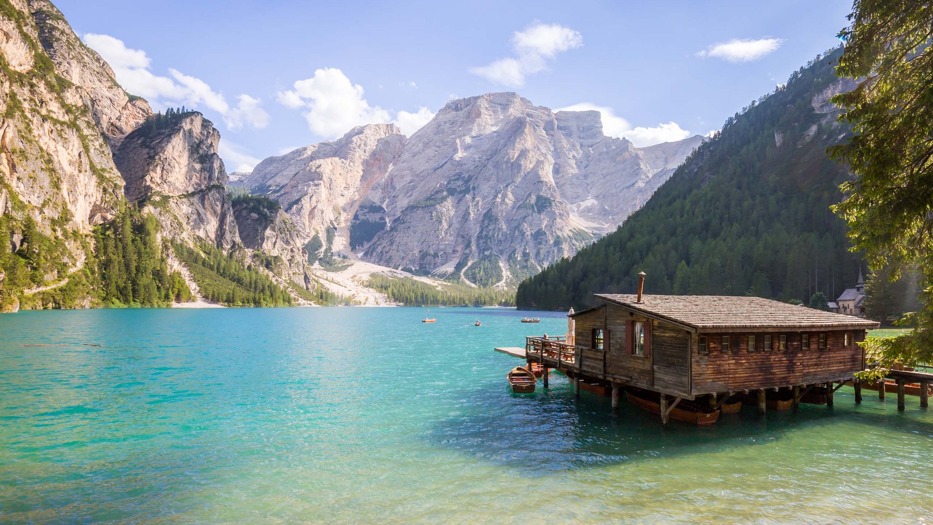 These attractions await you in Val Pusteria/Pustertal! Wooden house on turquoise lake with rocky mountains and forest background