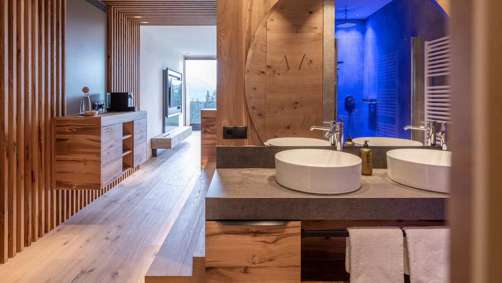 Le foto più belle dell’Alpen Tesitin Camera moderna con mobili in legno, bagno con doppio lavabo e doccia illuminata di blu